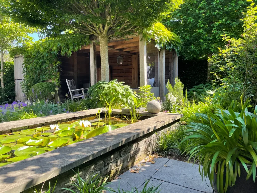 Groene tuin met vijver en terrasoverkapping. Deze tuin in ontworpen door de tuinarchitecten van Uw Tuin Hoveniers en aangelegd door de hoveniers van Uw Tuin Hoveniers uit Malden.