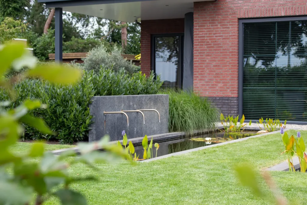 Vijver in de achtertuin van een moderne tuin in Middelaar met beplanting. Beplanting in de achtertuin van een moderne tuin in Mook. Deze tuin in ontworpen door de tuinarchitecten van Uw Tuin Hoveniers en aangelegd door de hoveniers van Uw Tuin Hoveniers uit Malden.